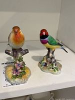 Two Staffordshire China bird figurines displayed on a flat surface, showing full figures of both birds including bases with floral detailing.