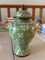 Front view of green cloisonné lidded vase with white leaf and floral pattern, showing shape and main decoration.