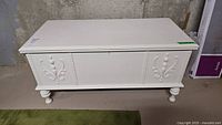 Front view of the white painted cedar chest showing decorative carved panels.