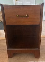 Front view of Knechtel wood side table showing drawer and open lower shelf, including brass handle on drawer and visible wood grain finish.