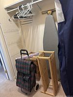 Photo showing wall-mounted ironing board, wooden shoe rack, plaid cloth buggy, and wicker hamper.