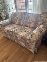 Full side view of the loveseat showing floral upholstery, attached cushions, and light wear on cushions.