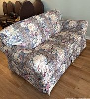 Full view of floral upholstered loveseat showing overall design, floral fabric, skirted base and attached top cushions.