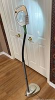 Full view of the magnifying floor lamp with flexible gooseneck and power supply cable, standing on a wooden floor in front of white doors.