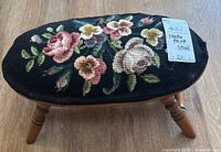 Front angled view of needlepoint stool showing floral upholstery and turned wooden legs.
