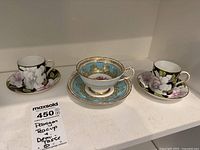 Three cups and saucers, including one blue Paragon teacup and saucer and two floral double warrant demitasse cups and saucers.