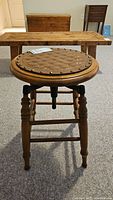 Front view of the antique wooden railway stool with decorative leather top and turned wood legs.