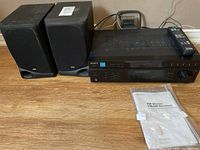 Full lot showing stereo receiver, two speakers, remote control, and instruction manual laid out on wooden surface.