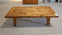 Front view of rectangular rustic reclaimed wood coffee table with solid plank top and angled legs.