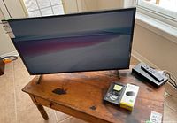 Full view of TV on bench with remote and accessory boxes