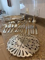 Full assortment of silver plated items laid out on countertop showing tray, cutlery, creamer, sugar, small vase, spoons, forks, knives, trivet and butter dish.