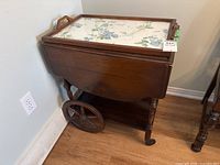 Wood tea cart stored with drop leaves folded down, showing wooden frame, castors and wheels.