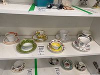 Photo displaying seven vintage teacups and their matching saucers arranged on a white shelf, showing styles and pattern variety