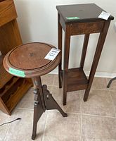 Two wooden plant stands shown together, one round pedestal stand and one tall rectangular stand with shelf.