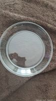 Top view of the clear glass pie dish showing the smooth circular rim and flat base, placed on a textured brown fabric.
