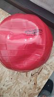 Red TheraBand silicone inflatable balance ball, partially inflated, showing logo and size details.