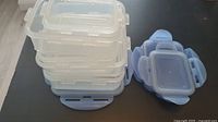 Stack of four clear rectangular plastic storage containers with light blue lids showing snap lock mechanisms.