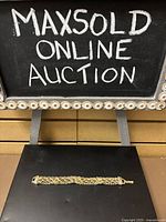Gold tone bracelet on black background with a chalkboard sign in background