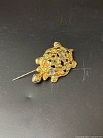 Top-side view of a vintage gold tone turtle brooch with colorful rhinestones set in a filigree shell pattern.