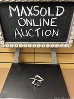 Photo showing the brooch on a black background beneath a sign reading 'MAXSOLD ONLINE AUCTION'