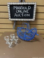 Overview of the blue wire duck-shaped egg basket and the four clear glass egg cups placed on a brown surface.