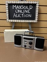 Photo of boombox with two speakers and white box behind it, on wooden brown surface