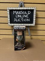 Front image of Duck Dynasty Phil Wacky Wobbler Talking Bobblehead in original packaging under a MAXSOLD online auction sign.