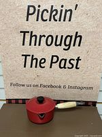 Full view of red Le Creuset enameled pot with wooden handle, black knob on lid, chip on lid handle visible.