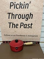 Full side view of red enameled cast iron saucepan with lid and wooden handle.