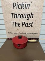 Red Le Creuset enameled cast iron saucepan with lid and wooden handle shown front view.