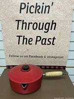 Full view of the red enameled cast iron saucepan with lid and wooden handle, photographed from the side.