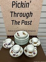 Front view of 12 luncheon plates stacked at center, four sandwich plates on top, and four teacups with saucers arranged around