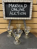 Set of four small honey/gold hue stemmed glasses arranged in front of a framed chalkboard
