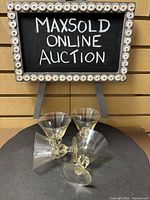 Four Swedish honey/gold hue stemmed glasses arranged on circular table under a sign reading 'MAXSOLD ONLINE AUCTION'.