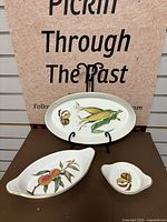 Three-piece set with oval platter, curved bowl, and a small dish, all fine porcelain with hand-painted botanical motifs.