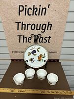 Porcelain plate with scalloped gold-trimmed edge and fruit design, along with four porcelain ramekins with matching fruit designs.