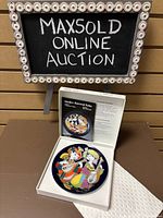 Photo of the closed decorative chalkboard with auction title and a table with the boxed plate visible.