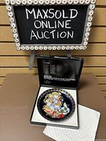 Photo shows the open box with the colorful aladin collector's plate inside, viewed from above with part of the box lid's text visible.