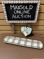 Rectangular ceramic serving dish and heart-shaped coasters displayed under a framed sign. The dish has a gray and white plaid design.
