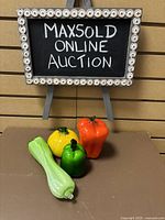 Photo showing all four blown glass vegetables together on a flat surface with a MaxSold Online Auction sign in background