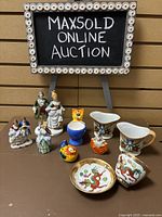 Overall view of collection including porcelain figurines, cream and sugar set, saki cup and saucer, and decorative cat figurine