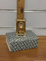 Full view of the mini clock standing on the original box with a ruler behind it indicating approximately 7 cm height.