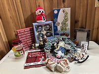 Wide view of lot showing most items including wreath, Santa figurines, ornaments, mugs, cookie jar, and signs.