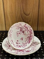 Close-up of the teacup showing detailed pink floral and bird design including peacock inside, displayed on matching saucer.