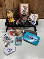 Full view of all collectible items arranged on a perforated black metal display stand and table including lion bank, NHL mugs, framed prints, playing cards, baseball, Pez dispenser, mini tea set and spoon