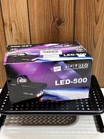 Photo showing the LED-500 fog machine box from one angle on a black perforated surface, showing front and top of box with branding and model number.