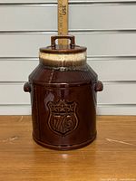 Full front view of brown McCoy cookie jar with 76 shield emblem and cream drip glaze effect at top, showing jar with lid and handles.