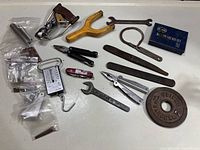 Overview of miscellaneous tools and hardware including wooden handle, pliers, wrench, spring, tuning forks, Swiss army knife, and small parts in bags