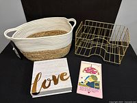 Photo showing the woven basket, brass-colored metal paper holder, vintage stationery pad, and decorative LOVE box arranged on a black surface.