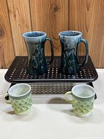 Two tall Quebec pottery mugs with bowling pin design on brown perforated surface, and two smaller green and white Kimberly Diamond mugs below